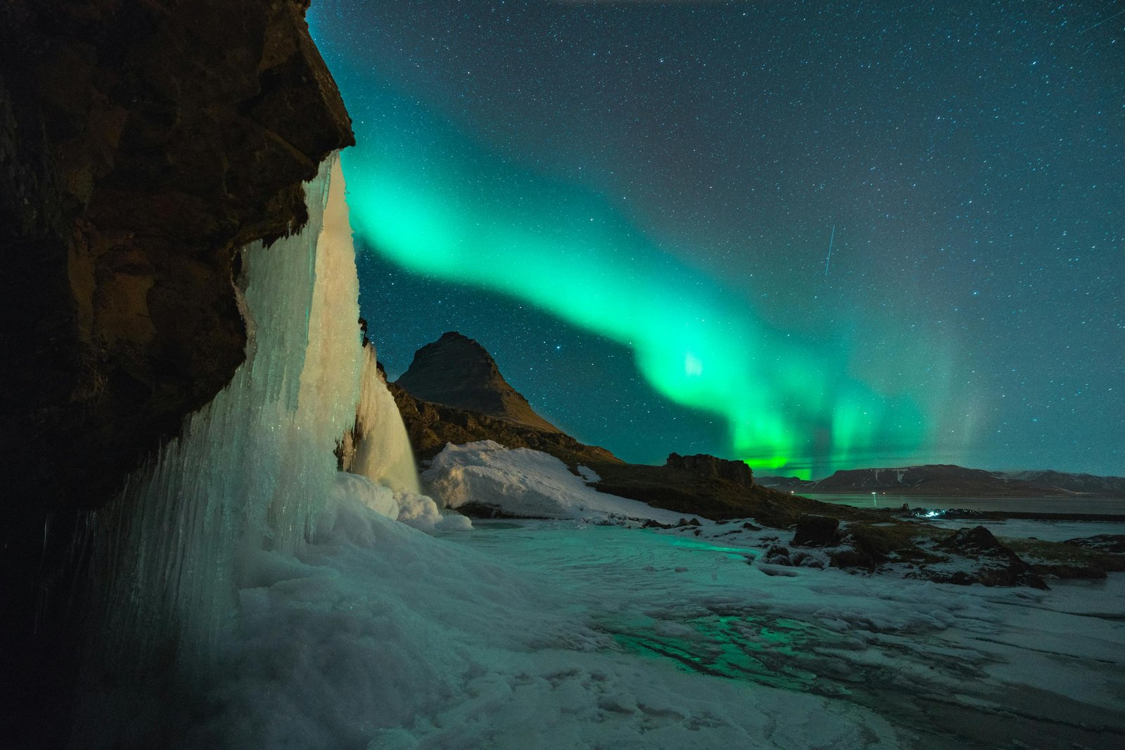 Green northern lights over a frozen waterfall, Thingvellir National Park, Iceland